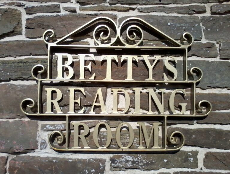 A fancy gold-coloured metal frame bearing the words 'Betty's Reading Room' is hung on a stone wall.